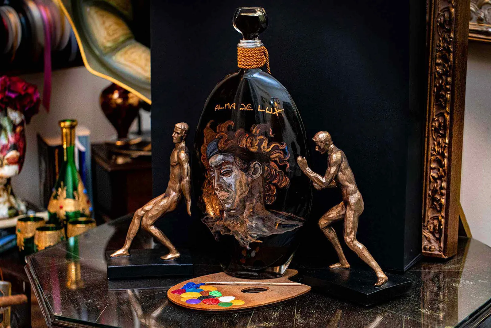 Bottiglia di liquore Alma De Lux dipinta a mano con un volto, tra due statuette in bronzo